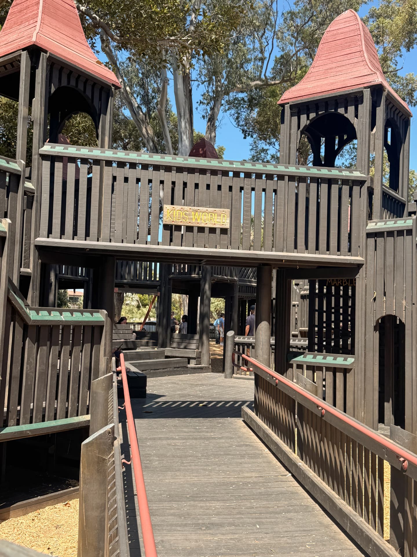 The wooden towers and ramp at the entrance of Kids World playground in Santa Barbara, with a carved Kids World sign