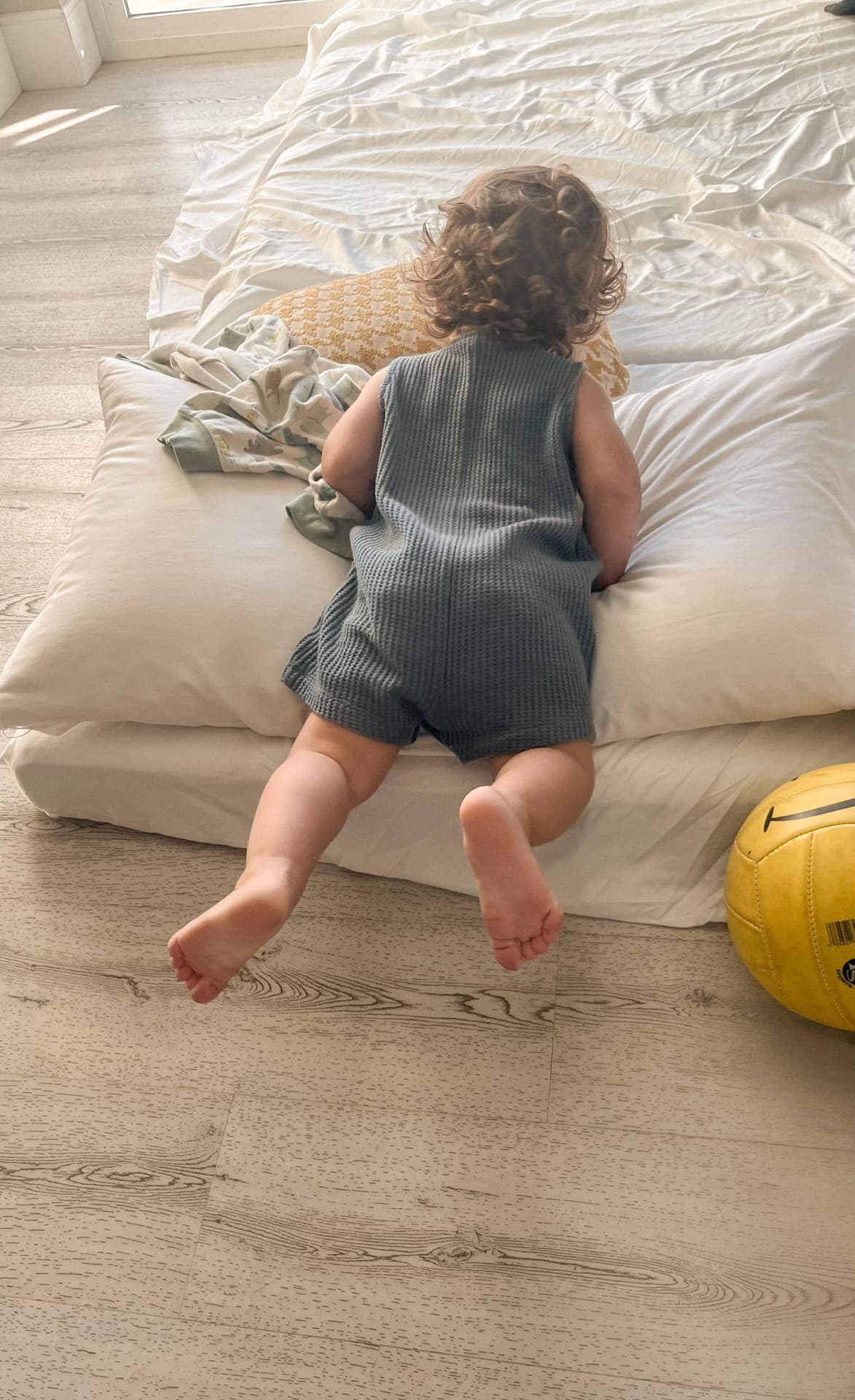 A toddler climbing onto the family's floor bed inside a hotel room
