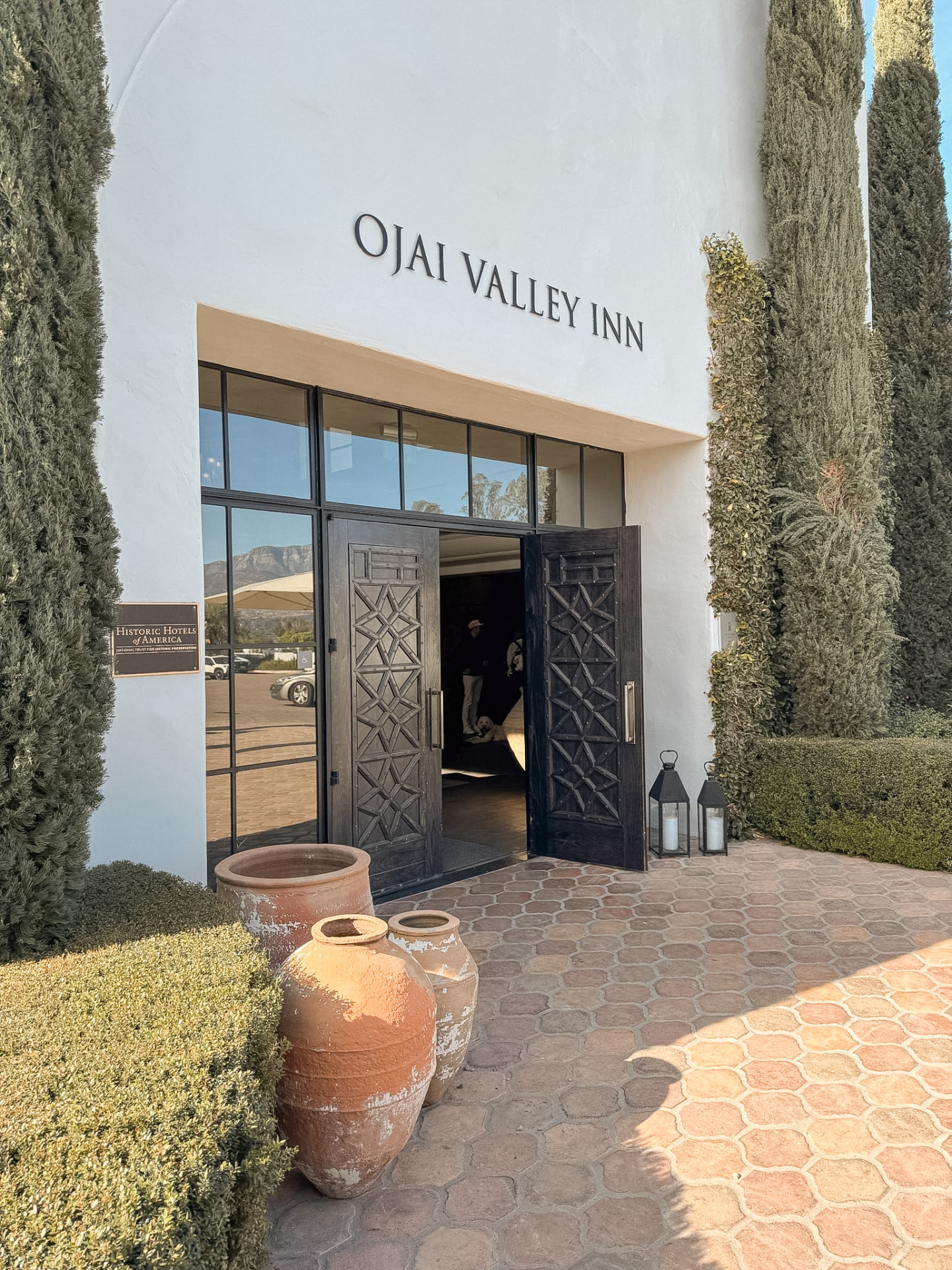 The white stucco entrance of Ojai Valley Inn with clay pots and cypress trees in flat afternoon light