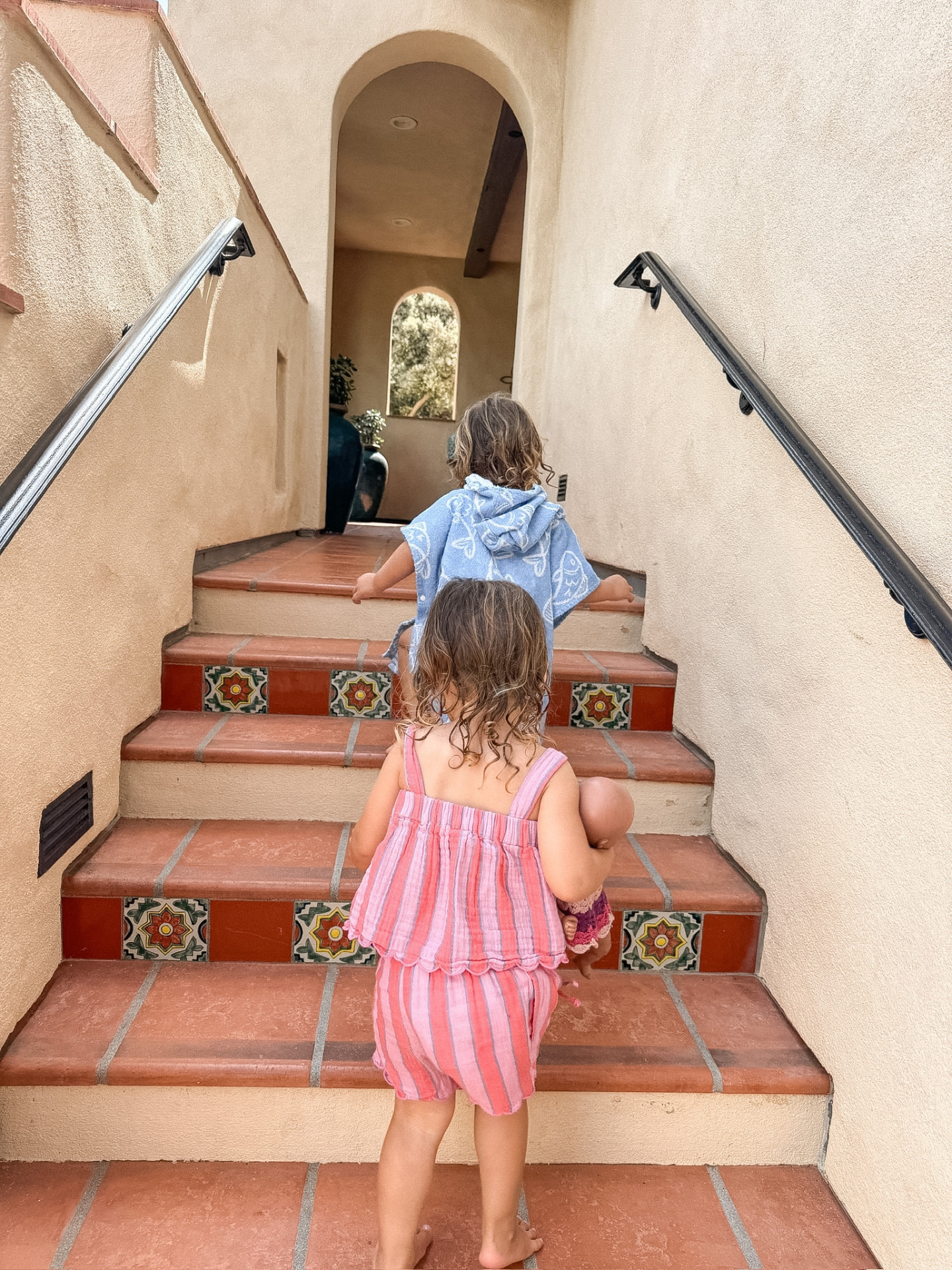 Our twins climbing a tiled resort staircase, one carrying a doll