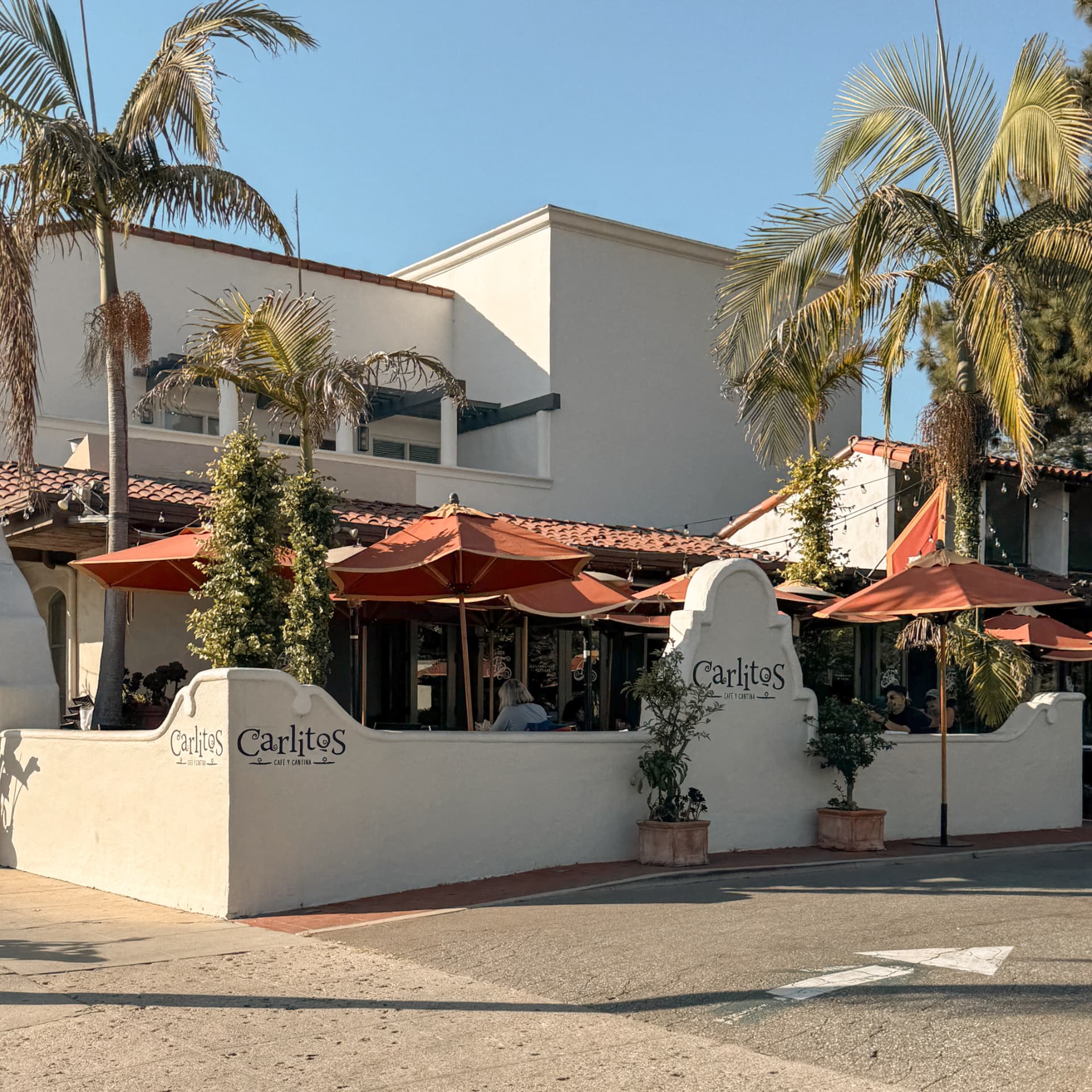 The white stucco exterior and terracotta patio umbrellas of Carlitos on Upper State Street, framed by palms