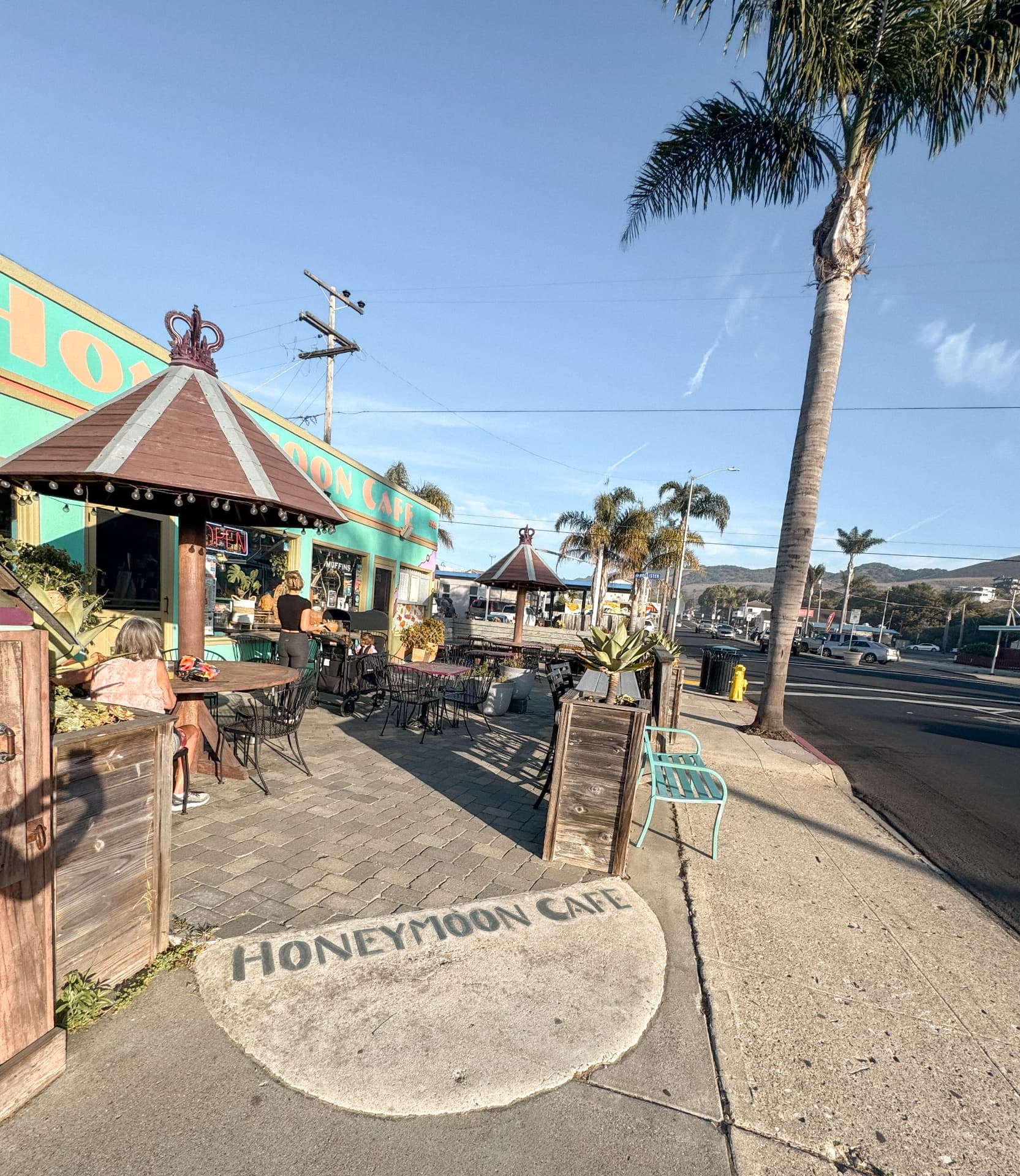 The turquoise exterior and outdoor patio seating at Honeymoon Cafe in Pismo Beach on a sunny morning