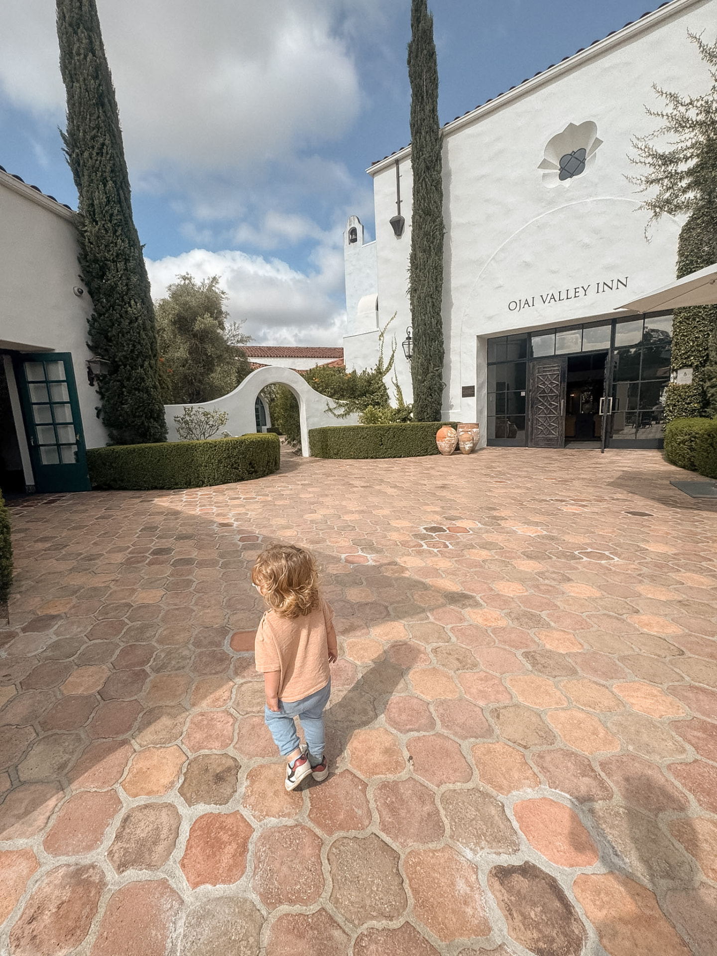 A toddler walking alone across the stone courtyard towards the entrance of Ojai Valley Inn