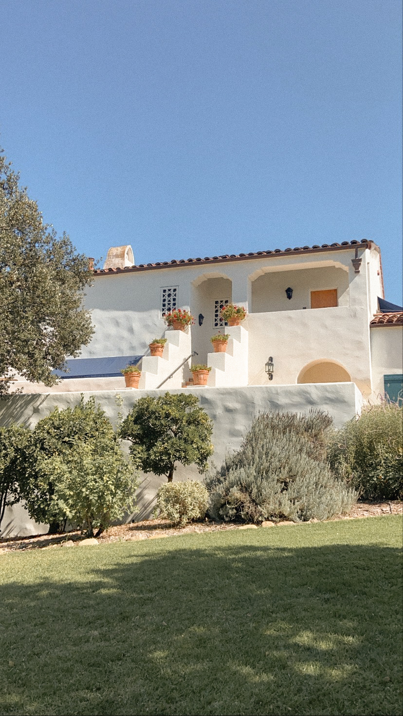A Spanish-style white villa with terracotta pots and a tiled roof above a lawn