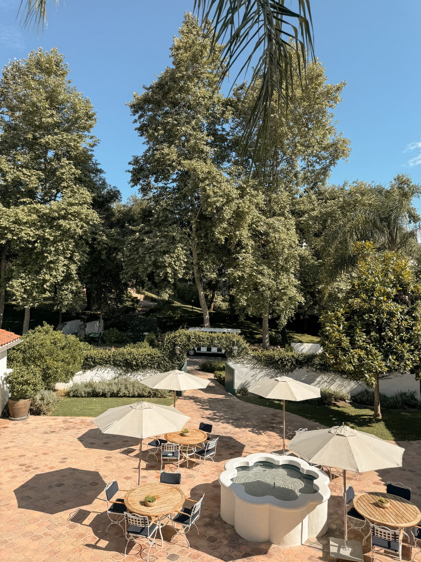 A quiet terracotta courtyard with cream umbrellas and a scalloped fountain before the day begins