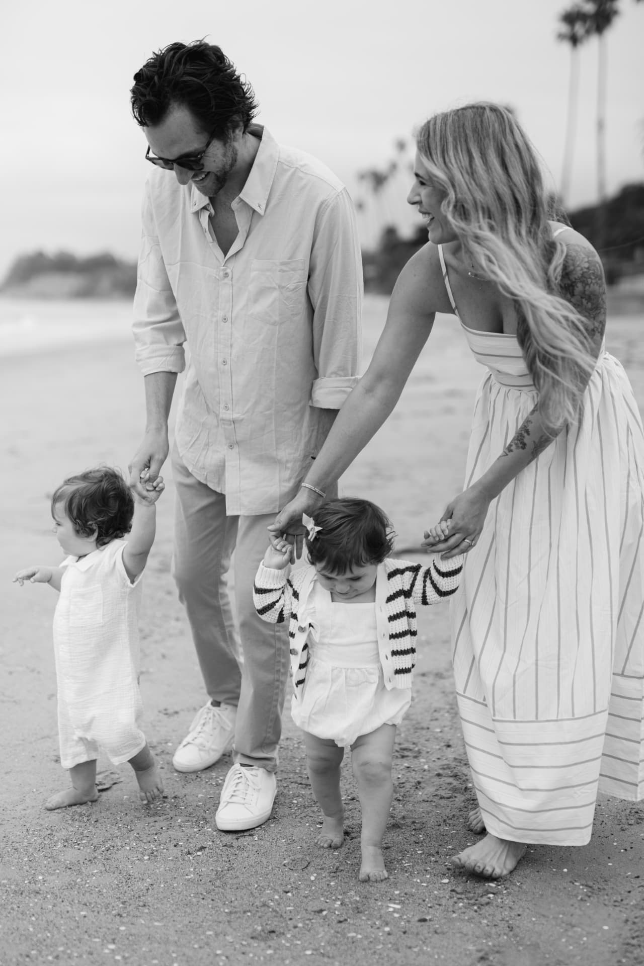 Armon and Linda Anderson walking on the beach hand in hand with their twins, in black and white