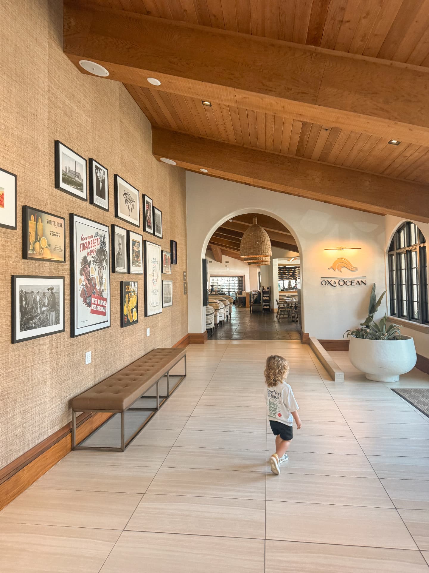 A small child walking alone down a wide hotel lobby toward the restaurant entrance