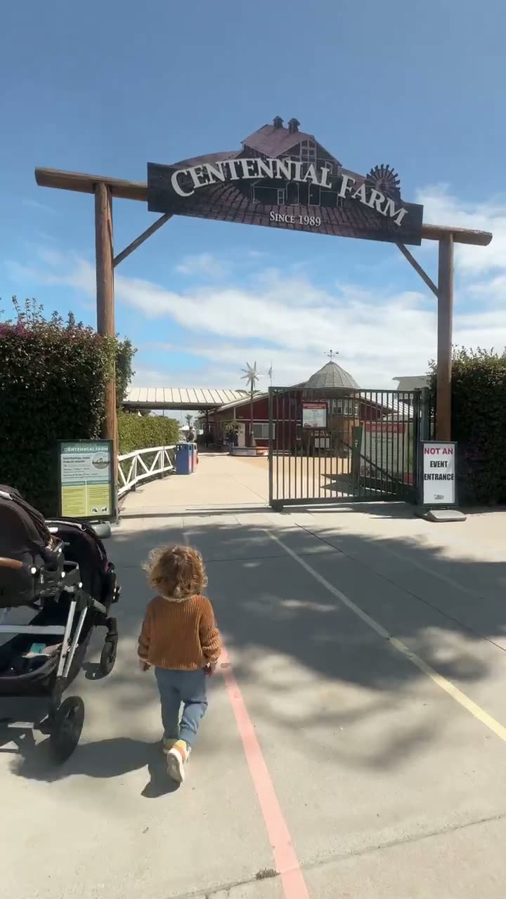 A short clip of a toddler walking ahead of the stroller under the Centennial Farm entrance sign in Costa Mesa