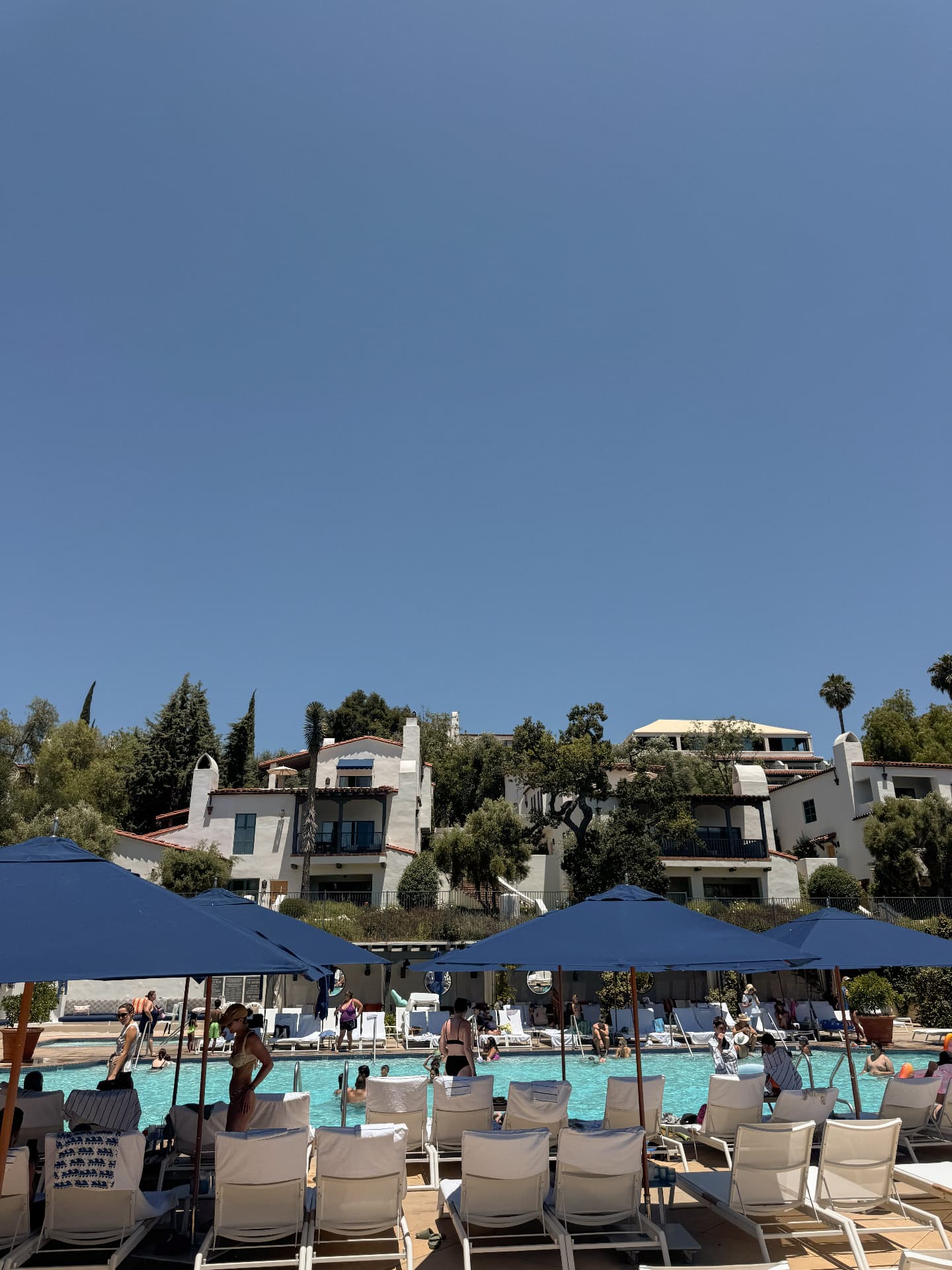 The main pool at Ojai Valley Inn under blue umbrellas, with Spanish-style buildings on the hill above